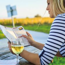 Dame trinkt Glas Weißwein und liest Neusiedler See Card Broschüre