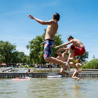 Kinder springen in den See, im Hintergrund Liegewiese
